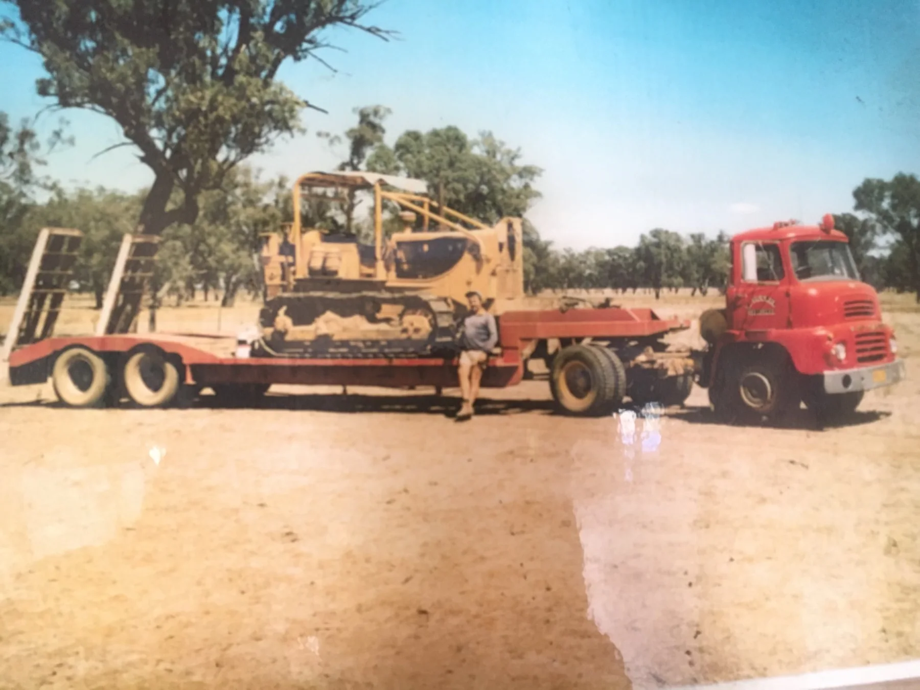 Historic red Huckel truck and low-loader carrying a tracked dozer